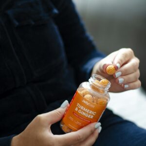 Person Holding an Orange Plastic Gummy Bottle