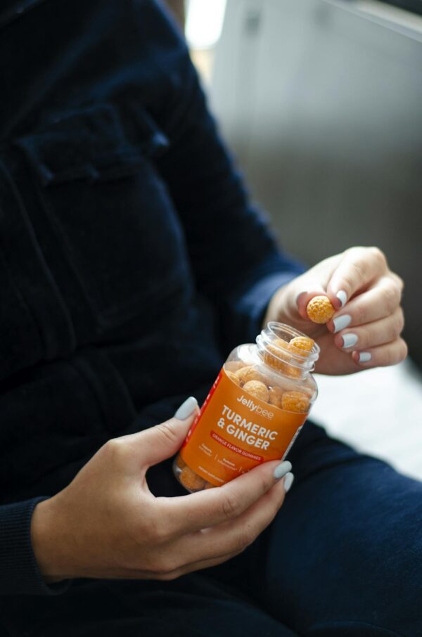 Person Holding an Orange Plastic Gummy Bottle